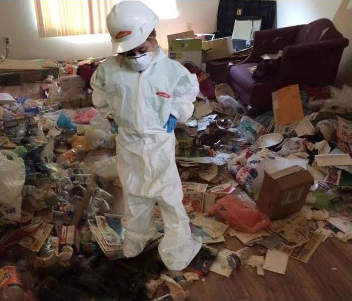young girl dressed in white hazmat suit standing in a room surrounded by garbage