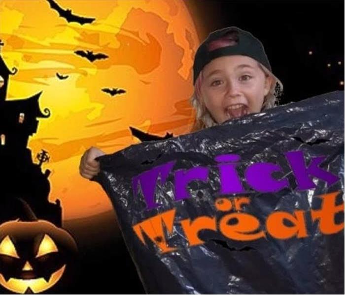 young girl standing in front of Halloween picture holding trick or treat bag