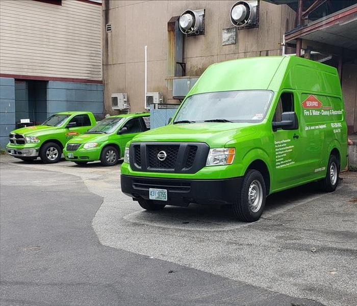 three bright green servpro work vehicles in front of business
